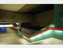 U-Bahn-Station mit Betonwänden, grün gefliesten Wandelementen und roten Handläufen. Der Bereich zeigt einen beleuchteten Treppenabgang sowie Bahnsteig-Schilder mit der Aufschrift „Schloßstraße“.