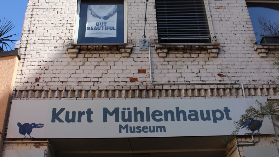 Fassade eines mehrstöckigen, weiß gestrichenen Backsteingebäudes mit Sprossenfenstern und dekorativen Ziegelbändern. Über einer breiten Durchfahrt hängt ein Schild mit der Aufschrift „Kurt Mühlenhaupt Museum“.
