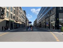 Breite Straße in einer Einkaufsgegend mit modernen und historischen Gebäuden; ein blaues U-Bahn-Schild mit der Aufschrift „Stadtmitte“ steht zentral auf einer Verkehrsinsel, flankiert von Geschäften wie Starbucks und Fußgängern.