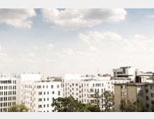 Städtische Landschaft mit modernen Wohngebäuden in Weiß und Beige, die von Bäumen umgeben sind. Der Himmel ist klar mit einigen Wolken.