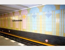U-Bahn-Station mit einer bunten Wandgestaltung aus pastellfarbenen Kacheln in Formen von Linien und geometrischen Mustern; der Stationsname „Kurfürstenstraße“ ist in schwarzer Schrift auf der Wand zu sehen. Die Gleise liegen vor einer unteren Wand aus dunklen Ziegelsteinen.