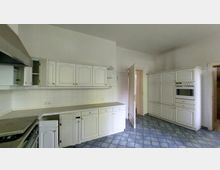 Klassische Küche mit weißen, verzierten Einbauküchenschränken, eingebautem Backofen und Herd. Der Boden ist mit blauen, geschwungenen Fliesen gestaltet, und die Wände sind teils mit weißen Fliesen verkleidet.