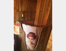 Duschbereich in rustikalem Holzdesign mit einer Duschvorhang-Abbildung eines klassischen Porträts einer Frau. Die Wandverkleidung und Umgebung bestehen vollständig aus warmem Holzmaterial.