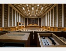 Innenraum eines Konzertsaals mit hölzernem Design, einer zentralen Bühne mit Orgel im Hintergrund und gestuften Sitzreihen. Die Wände sind mit hohen Säulen und rechteckigen, vergitterten Akustikpaneelen gestaltet, die Decke ist mit einem geometrischen Muster versehen.