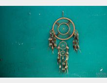 Ein großer Traumfänger mit Holzrahmen und Federn hängt an einer türkisfarbenen, leicht abgenutzten Wand.