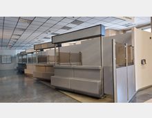 Innenraum eines öffentlichen Verwaltungsgebäudes mit einer Reihe von grauen Schaltern und transparenten Trennwänden. Der Raum hat eine Decke mit Rasterleuchten und einen Boden aus glänzendem Stein.