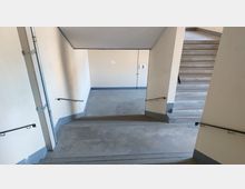 Treppenhaus mit mehreren Treppenabsätzen und beige gestrichenen Wänden. An den Treppen befinden sich schwarze Handläufe, und die Stufe "3" ist an der Wand markiert.