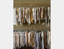 Viele Papiervorlagen und Muster aus hellem und braunem Papier hängen geordnet an Drahtbügeln, die an zwei horizontalen Metallstangen befestigt sind, vor einer beigefarbenen Wand.