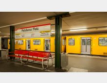 U-Bahnhof mit gelbem Zug der Linie U2 am Potsdamer Platz in Berlin. Im Vordergrund stehen eine rote Sitzbank und Hinweisschilder, während im Hintergrund die Zugtüren zum Ein- und Aussteigen geöffnet sind.