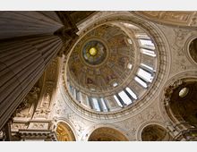 Blick nach oben in eine reich verzierte Kuppel eines historischen Kirchengebäudes mit kunstvollen Fresken, goldenen Dekorationen, Säulen und großen Fenstern, die Tageslicht hereinlassen.