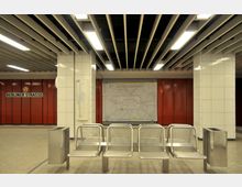 U-Bahn-Station mit modernem Design: Sitzbänke aus Metall in der Mitte, umgeben von weißen gefliesten Säulen und roten Wandpaneelen. Eine große Netzplan-Tafel und das Schild „Berliner Straße“ sind sichtbar.