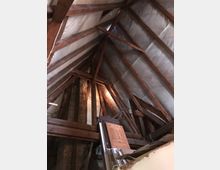 Dachboden mit sichtbarer Holzbalkenkonstruktion und isolierten Dachflächen. Im Vordergrund liegen Holzpaneele, Türen und Baumaterialien.