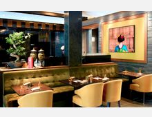 Elegantes Restaurant mit moderner asiatischer Einrichtung, einschließlich gepolsterter Sitzbänke, Holztischen und beigefarbenen Stühlen. Im Hintergrund ein Bonsai-Baum, dekorative Vasen und ein Bild einer traditionellen Geisha, umrahmt von einer gelben Wand mit Steinakzenten.