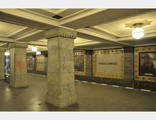 U-Bahn-Station mit Säulen aus grauem Stein, gefliesten Wänden und Wandtafeln, auf denen „Hohenzollernplatz“ steht. Helle Deckenleuchten und ein Uhranzeiger ergänzen das Ambiente.