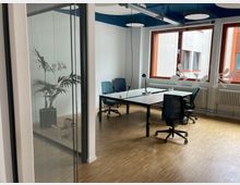 Moderner Besprechungsraum mit einem großen rechteckigen Tisch, mehreren Bürostühlen und einer Glastür. Der Raum hat helle Holzböden, große Fenster mit Blick nach draußen, eine Zimmerpflanze in der Ecke und dekorative Elemente auf der Glaswand.