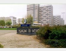 Eingang zur U-Bahn-Station „Spittelmarkt“ in Berlin, umgeben von Grünflächen und Gehwegen, mit Hochhäusern und moderner Architektur im Hintergrund.