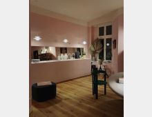 Modern eingerichtete Küche mit pastellrosa Wänden und passenden Küchenmöbeln. Der Raum verfügt über Holzfußboden, eine Fensterfront, minimalistische Pendelleuchten und dekorative Elemente wie Vasen, Kunstgegenstände und Pflanzen.