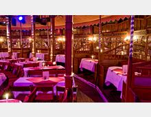 Innenansicht eines historischen Spiegelzelts mit Holzelementen, Spiegelwänden und gedämpfter Beleuchtung. Rote Tischdecken und Kerzen auf weiß eingedeckten Tischen schaffen eine stimmungsvolle, nostalgische Atmosphäre.