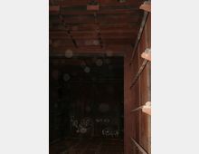 Innenansicht eines rostigen, verlassenen Metallcontainers oder Industriegebäudes mit Stahlträgern an der Decke und Graffiti an den Wänden. Der Raum wirkt dunkel, und Staubpartikel sind deutlich zu erkennen.