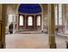 Innenraum einer verlassenen Kirche mit einer kleinen Kanzel links, halbkreisförmigen Fenstern und einer gebogenen Apsis mit einem blauen Sternenhimmel. Die Wände sind abblätternd, der Boden besteht aus alten Ziegelsteinen, und die allgemeine Atmosphäre ist verwittert.