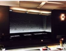 Ein modernes Restaurant oder eine Bar mit dunkler Beleuchtung, Sitznischen entlang einer weißen Backsteinwand im Hintergrund und einer Theke im Vordergrund mit Gläsern und Barutensilien.