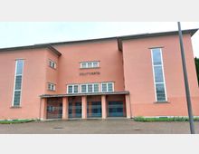 Außenansicht eines rosa gestrichenen Gebäudes mit der Aufschrift „Stadttheater“ über dem Eingang. Das Gebäude hat hohe schmale Fenster an den Seiten sowie mehrere verschlossene Eingangstüren mit Gittertoren.