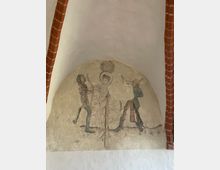 Wandfresko in einer gewölbten Nische mit rotem Ziegelsteinrahmen, das eine mittelalterliche Darstellung zeigt: eine zentral stehende Figur mit Heiligenschein wird von zwei Figuren mit Bögen angegriffen. Der Hintergrund ist hell und schlicht.