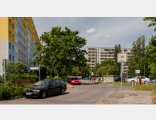 Wohnviertel mit mehrstöckigen Wohngebäuden, umgeben von Bäumen und Grünflächen. Im Vordergrund eine Straße mit parkenden Autos, Verkehrsschildern und einem Gehweg, daneben ein Schild, das eine Tempo-30-Zone anzeigt.