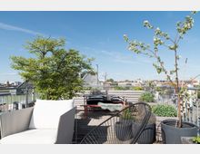 Dachterrasse mit Holzfußboden und Pflanzen in Blumenkübeln, möbliert mit einem weißen Sessel, einem Tisch, Bänken und Stühlen. Im Hintergrund sind städtische Gebäude und ein klarer blauer Himmel zu sehen.