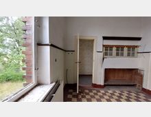 Ein leerer Raum mit abgewittertem Charme, gekennzeichnet durch einen karierten Boden aus beige-braunen Fliesen, eine offene Tür zu einem angrenzenden Zimmer und eine Nische mit kleinen Fenstern. Links befindet sich ein großes, offenes Fenster mit Blick ins Grüne, dessen Rahmen teils aus Ziegelsteinen besteht.