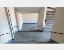 Treppenhaus mit Betonstufen und gelbem Anstrich an den Wänden. Handläufe befinden sich an beiden Seiten, und die Wand zeigt eine Etage-Markierung mit der Zahl „3“.