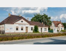 Ein kleines, einstöckiges Bahnhofsgebäude mit der Aufschrift „Premnitz Süd“ und verputzter Außenfassade, teils mit Graffiti, steht an einer Straße; im Hintergrund sind weitere Wohnhäuser und Bäume zu sehen.