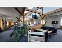 Ein heller Bibliotheksraum mit hohen Decken, sichtbaren Holzbalken und großen Fenstern. Links stehen Regale mit Büchern, in der Mitte befinden sich Arbeitsplätze, und rechts ist eine Sitzecke mit Sofas und Tischen.