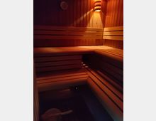 Holzverkleideter Innenraum einer Sauna mit Bänken aus Holz, sanfter Beleuchtung an der Wand und einem Wassereimer mit Schöpfkelle auf dem Boden.