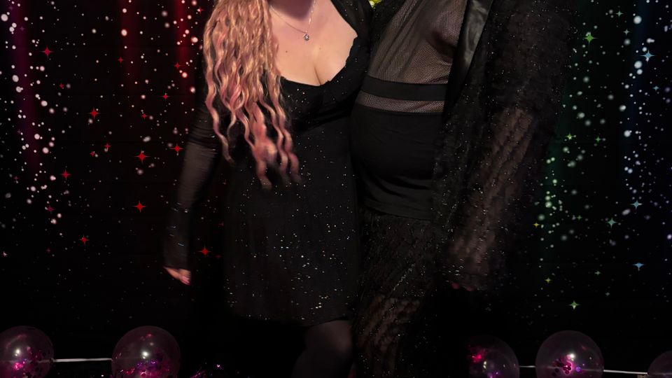 Indoor photo booth setup with a rainbow-striped, star-speckled backdrop and a pink floor, decorated with scattered balloons and tinsel along the base.