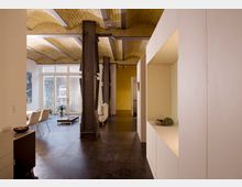 Wohnraum in einem renovierten Industrieloft mit hohen gewölbten Ziegeldecken, Stahlträgern und großen Fenstern, die viel Tageslicht einlassen. Der Raum verfügt über moderne Möbel, glatte dunkle Holzböden und helle, minimalistische Einbauelemente.