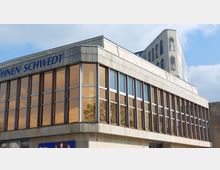 Außenansicht eines modernen Theatergebäudes mit der Aufschrift „Bühnen Schwedt“. Das Gebäude hat eine Fassade aus hellen Steinplatten und große, braun getönte Fenster; im oberen Bereich ist ein Turm mit bemalten Figurenfenstern sichtbar.