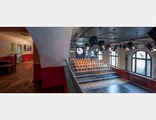 Ein kleiner Theatersaal mit ansteigender Sitztribüne aus Holzstühlen, umgeben von einer Wand mit großen Rundbogenfenstern. Über der Tribüne befinden sich Scheinwerfer und Lichttechnik, der Boden besteht aus dunklem Holzparkett.