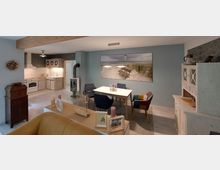 Gemütlicher Wohn- und Essbereich mit offener Landhausküche, einem Esstisch mit bunten Stühlen, einem modernen Kaminofen und einer Wanddekoration mit Strandmotiv. Rechts steht eine helle Vitrine im Vintage-Stil, links ein braunes Holzregal.