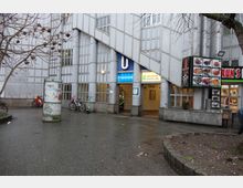 Eingang einer U-Bahn-Station mit der Aufschrift „Prinzstraße” und Wegweisern zu den Linien U1 und U3. Das Gebäude hat eine moderne Glas- und Betonfassade, daneben befinden sich eine Litfaßsäule, abgestellte Fahrräder und ein Imbiss mit einer Speisekarte außen an der Wand.