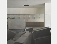 Ein leerer Garderobenbereich mit nummerierten Kleiderhaken (1-200) an der Wand, teilweise verdeckt durch gestapelte Metallteile. Die Umgebung wirkt unfertig oder im Umbau.