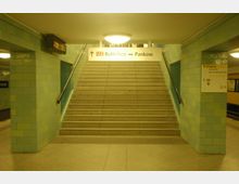 Treppenaufgang in einer U-Bahn-Station mit grünen Kacheln an den Wänden. Oben befindet sich ein Schild mit der Beschriftung „U2 Ruhleben ↔ Pankow“, daneben ein Hinweisschild für den Ausgang.
