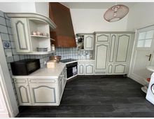 Traditionelle Küche mit cremefarbenen Schränken, blauen Akzenten und einem dunklen Fliesenboden. Kupferfarbene Dunstabzugshaube, helle Wandfliesen und eine schlichte Hängelampe ergänzen das Design.