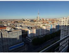 Blick über Berlin mit mehreren Wohngebäuden und Bürohäusern im Vordergrund. Im Hintergrund sind der Berliner Fernsehturm, der Berliner Dom und weitere historische Gebäude und Wahrzeichen zu sehen, unter klarem Himmel.