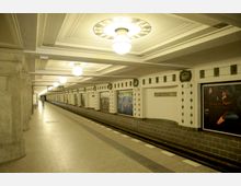 U-Bahn-Station mit heller Deckenbeleuchtung und kunstvollen Verzierungen. Auf den Wänden befinden sich dekorative Elemente und Kunstwerke, während der Bahnsteig leer ist. Ein Schild zeigt den Namen "Rüdesheimer Platz".