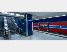 U-Bahn-Station mit zwei Rolltreppen und blau gefliesten Wänden, daneben eine rot-blau-weiße Wandverkleidung mit der Aufschrift „Osloer Straße“. Ein Schild mit dem Hinweis „Ausgang“ ist oberhalb der Rolltreppen angebracht.