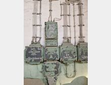 Metallene Schaltkästen mit abblätternder grüner Farbe und handgeschriebenen Beschriftungen, montiert an einer weißen, teilweise beschädigten Wand. Mehrere Kabelbinder bündeln elektrische Leitungen, die zu und von den Kästen führen.
