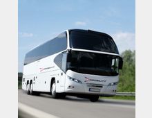 Ein moderner weißer Reisebus mit dem Logo „BMobility“ fährt auf einer Straße, umgeben von einer ländlichen Landschaft unter klarem Himmel. Der Bus hat eine aerodynamische Front und breite Seitenscheiben.