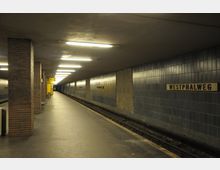 Unterirdische U-Bahn-Station mit dunklen Fliesenwänden, Deckenbeleuchtung und einem schmalen Bahnsteig neben den Schienen. Ein Schild mit der Aufschrift „Westphalweg“ ist an der Wand angebracht.