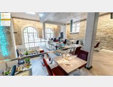 Restaurant mit modernem Design und historischem Flair, gekennzeichnet durch freiliegende Ziegelwände und große bogenförmige Fenster. Der Raum ist auf zwei Ebenen angelegt und verfügt über elegant gedeckte Tische, eine offene Decke und zeitgenössische Beleuchtung.